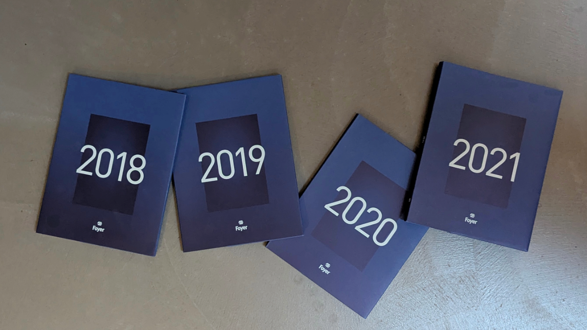 Quatre rapports annuels FOYER disposés sur un fond plat gris.
