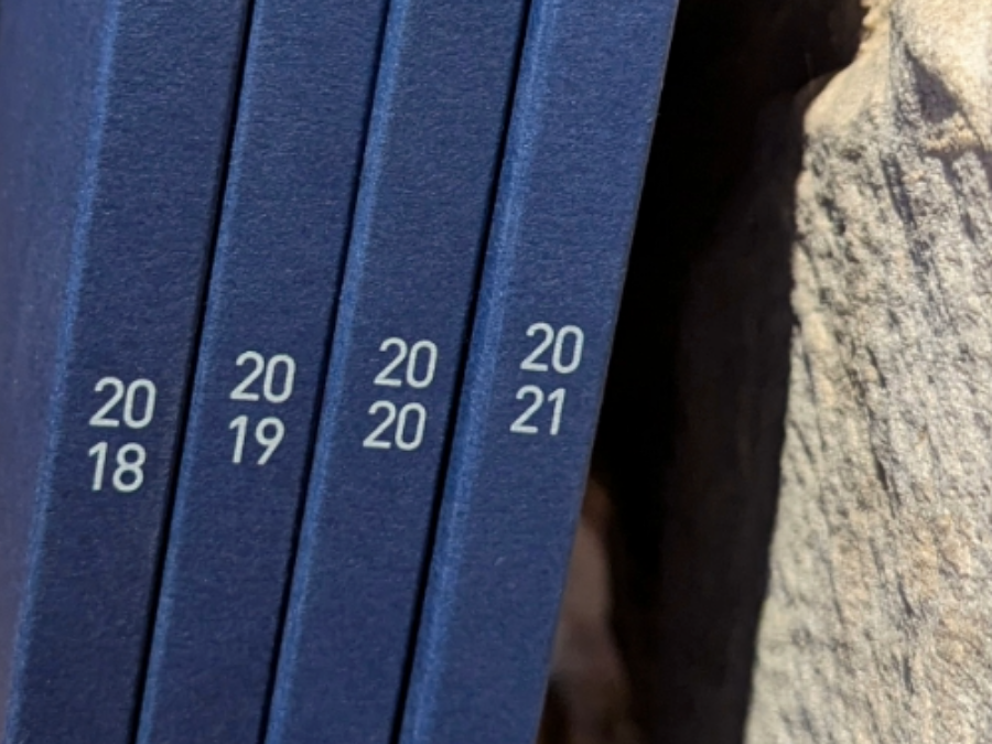 4 rapports annuels Foyer 2018-2019-2020-2021, posés sur une étagère, l'on aperçoit les tranches avec les années.