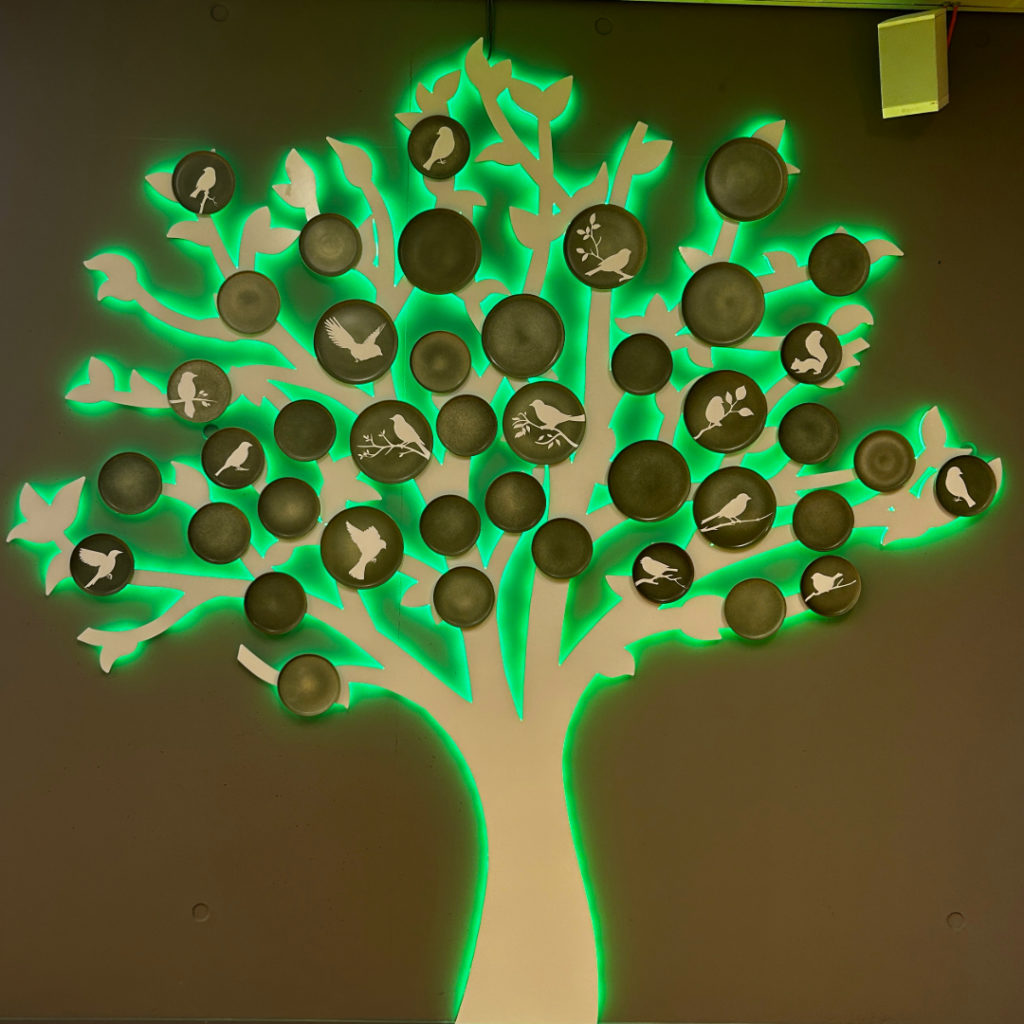Décoration murale en forme d’arbre avec branches lumineuses vertes et disques illustrés d’animaux.