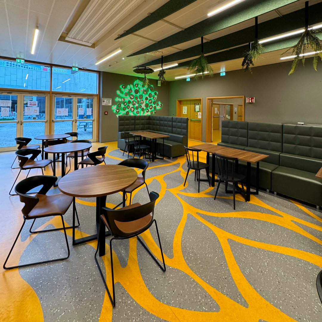 Espace collectif décoré avec chaises modernes, motifs de branches au sol, et un arbre mural lumineux symbolisant la croissance et la collectivité.