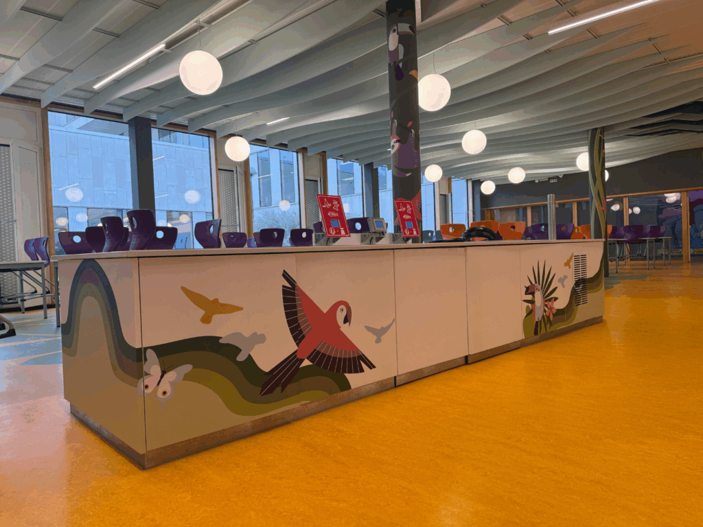 Comptoir de cafétéria décoré d’illustrations d’oiseaux et d’animaux colorés, avec chaises violettes en arrière-plan.