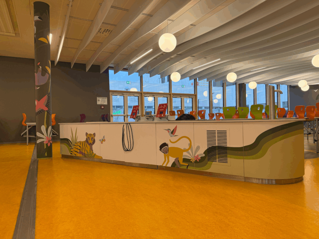 Comptoir de cafétéria décoré d’illustrations colorées d’animaux, dont un tigre et un singe, avec chaises orange visibles en arrière-plan.