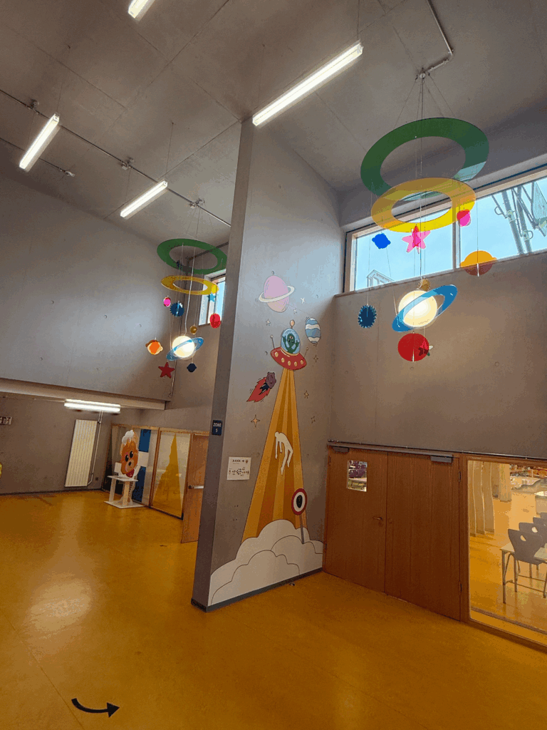 Salle décorée sur le thème de l’espace avec fusée peinte, planètes suspendues au plafond et fresque murale cosmique.