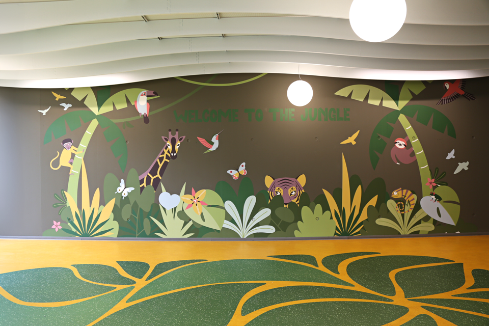 Fresque murale jungle avec girafe, tigre, singe, oiseaux et papillons, sur fond de végétation tropicale avec l’inscription Welcome to the Jungle.