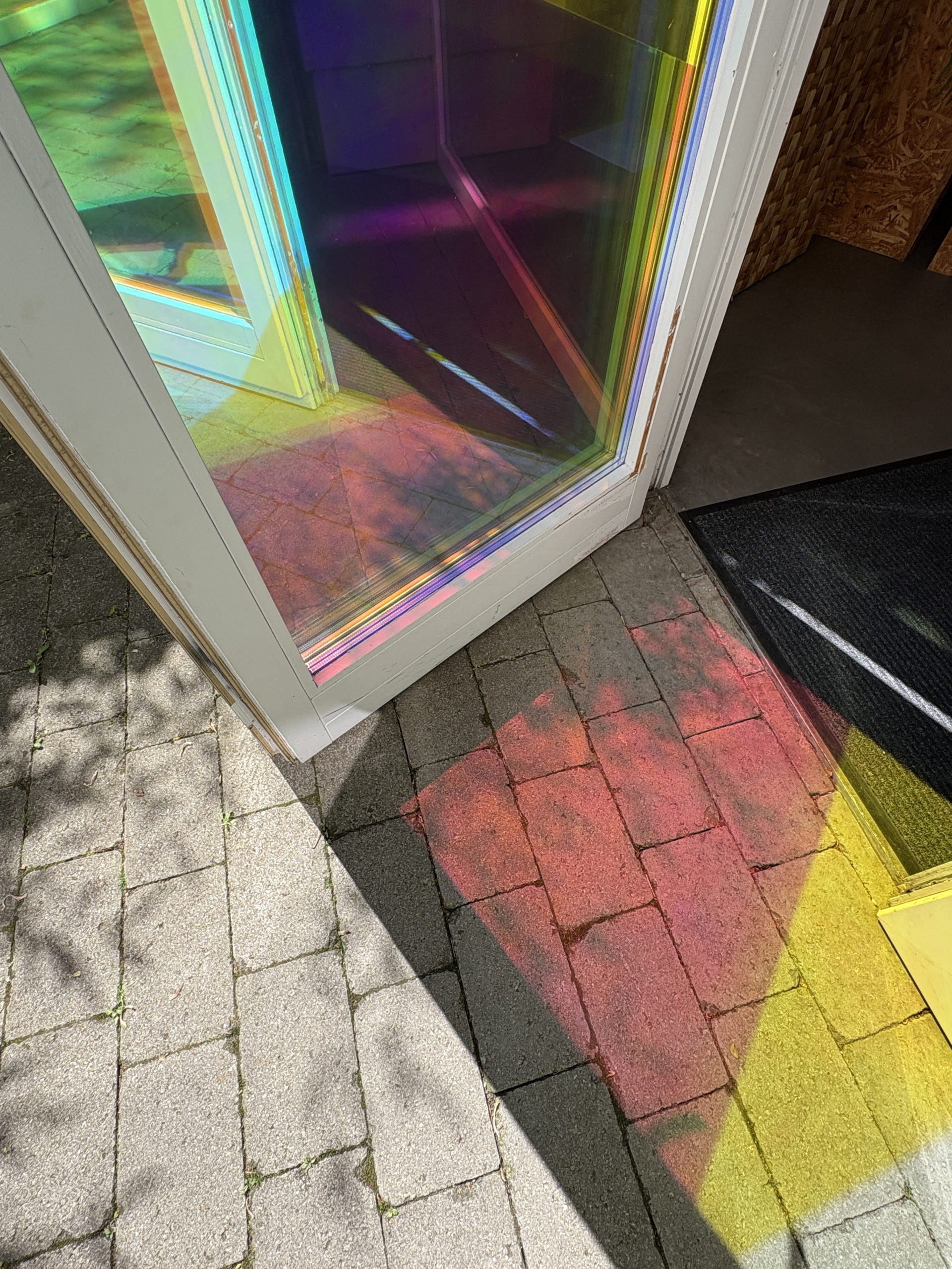 Photographie d’une porte d'entrée ouverte, vu sol avec reflets rouge et jaune