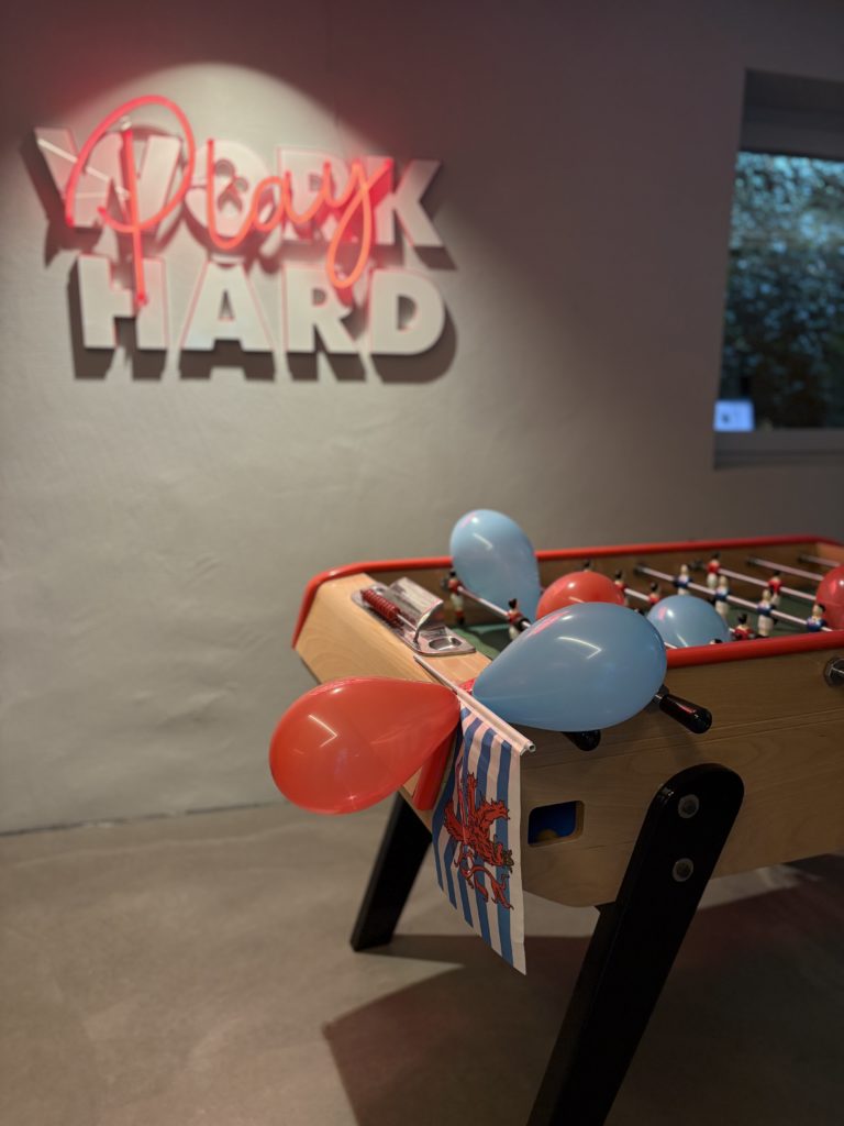 Baby-foot décoré de ballons et d’un drapeau luxembourgeois, néon « Work Play Hard » au mur