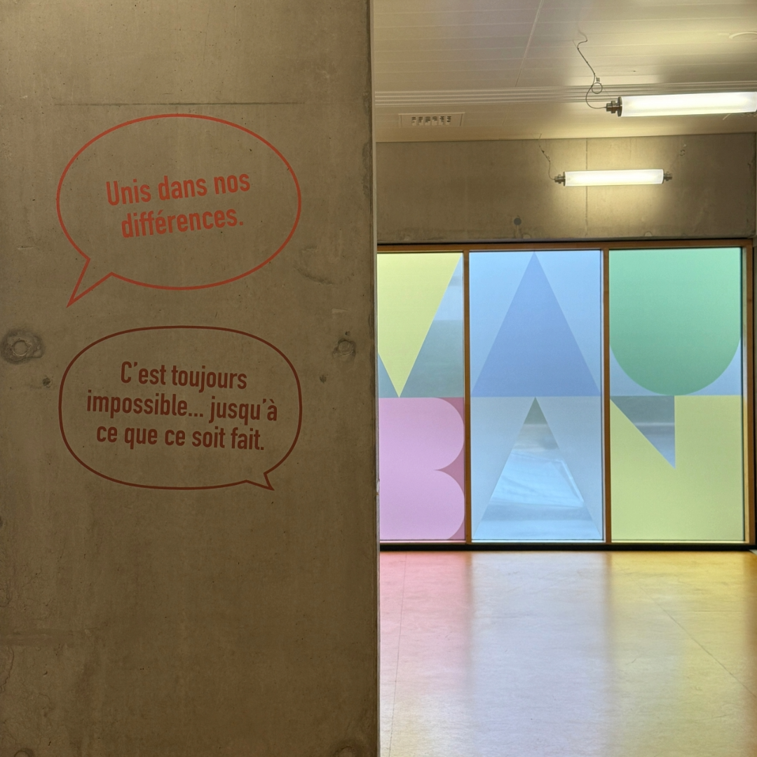 Mur en béton avec deux bulles de texte : « Unis dans nos différences. » et « C’est toujours impossible… jusqu’à ce que ce soit fait. » ; vitres au fond avec lettrage coloré « VAUBAN