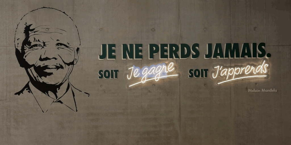 Portrait de Nelson Mandela en noir sur un mur gris, avec la phrase : "Je ne perds jamais. Soit je gagne, soit j'apprends."