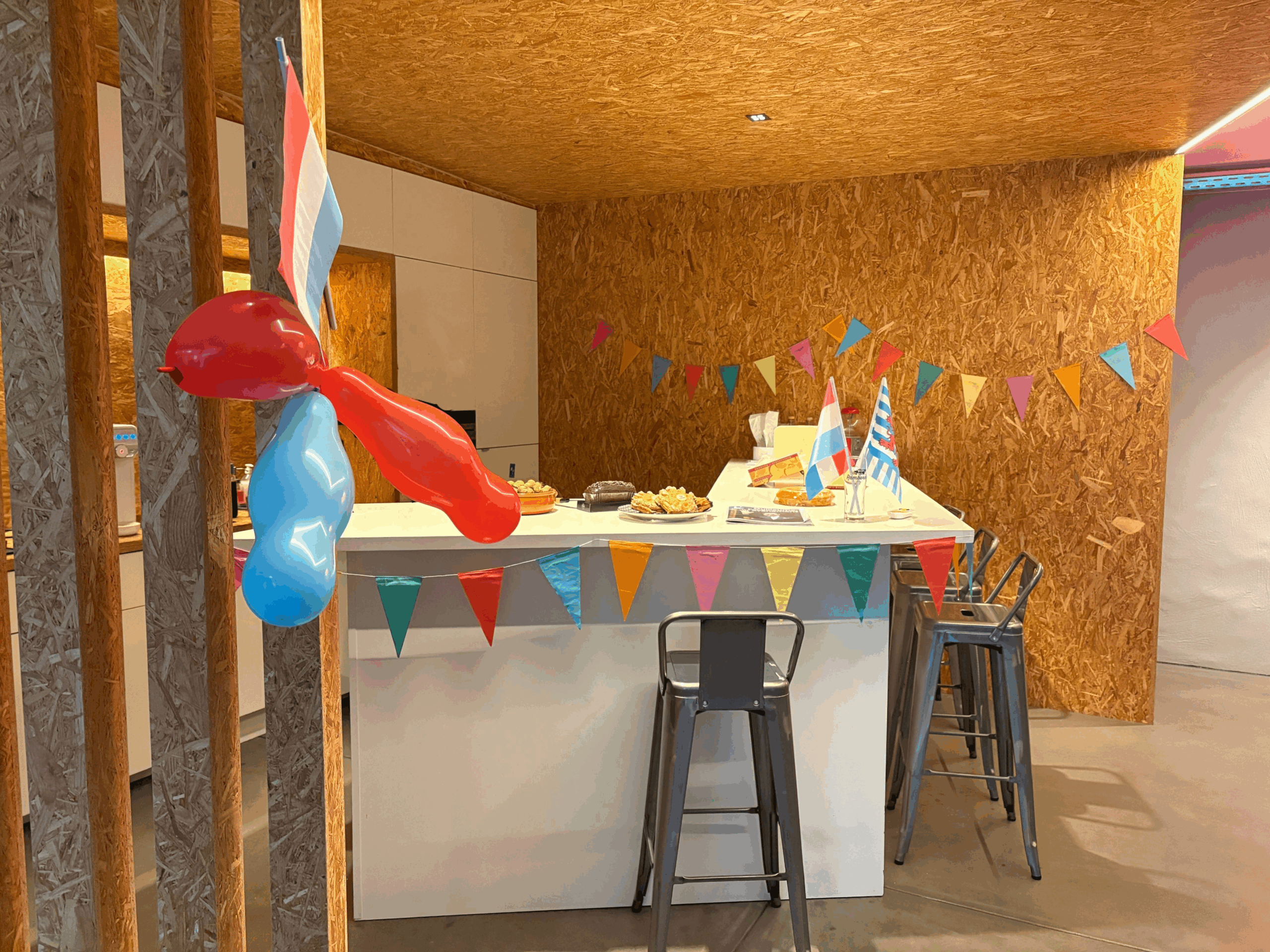 Comptoir décoré pour fête : fanions multicolores, ballons rouge et bleu, drapeaux luxembourgeois
