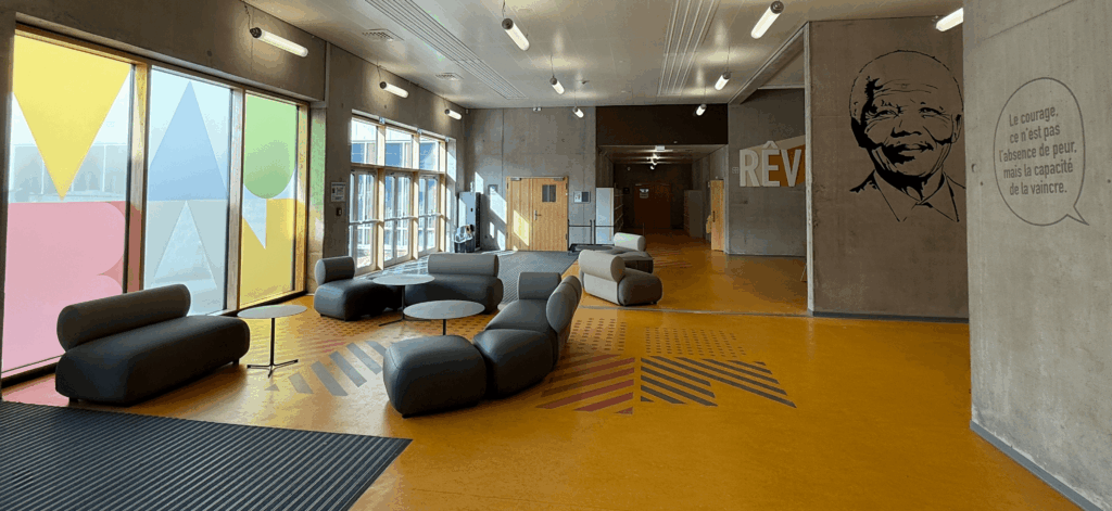 Espace d’accueil lumineux avec canapés, vitres décorées de formes colorées et portrait de Nelson Mandela sur le mur.