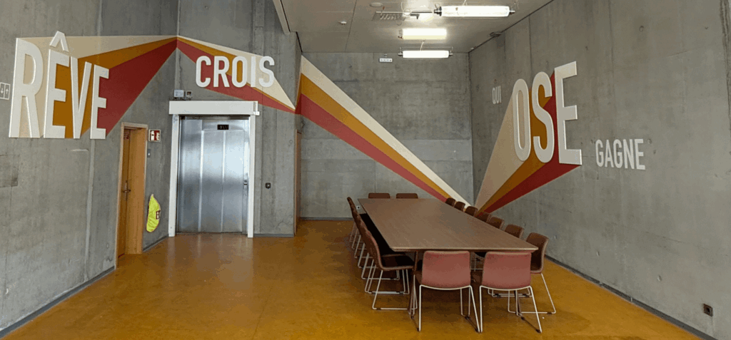 "Salle de réunion avec longue table en bois et fresque murale RÊVE CROIS OSE GAGNE.