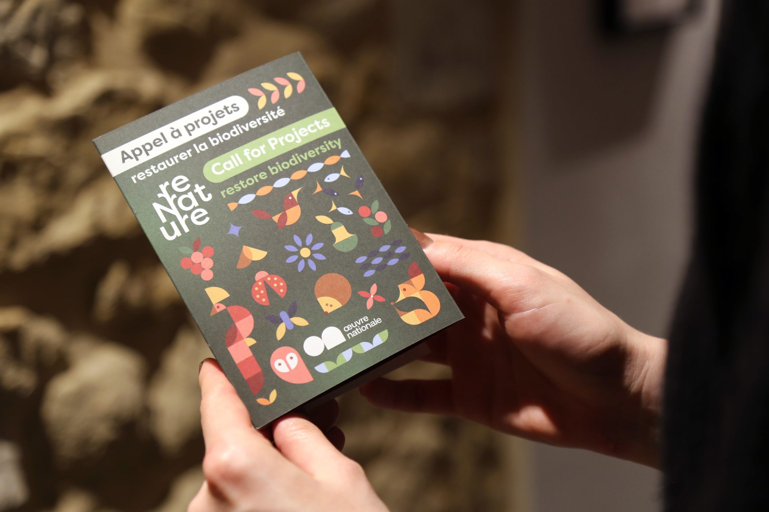 Personne tenant dans les mains la brochure ReNature présentant un appel à projets pour restaurer la biodiversité.