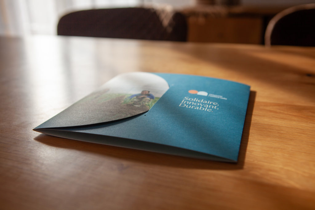 Dépliant fermé posé sur une table en bois, avec la couverture bleu foncé affichant le logo de l’Œuvre Nationale et le slogan “Solidaire, Innovant, Durable”.