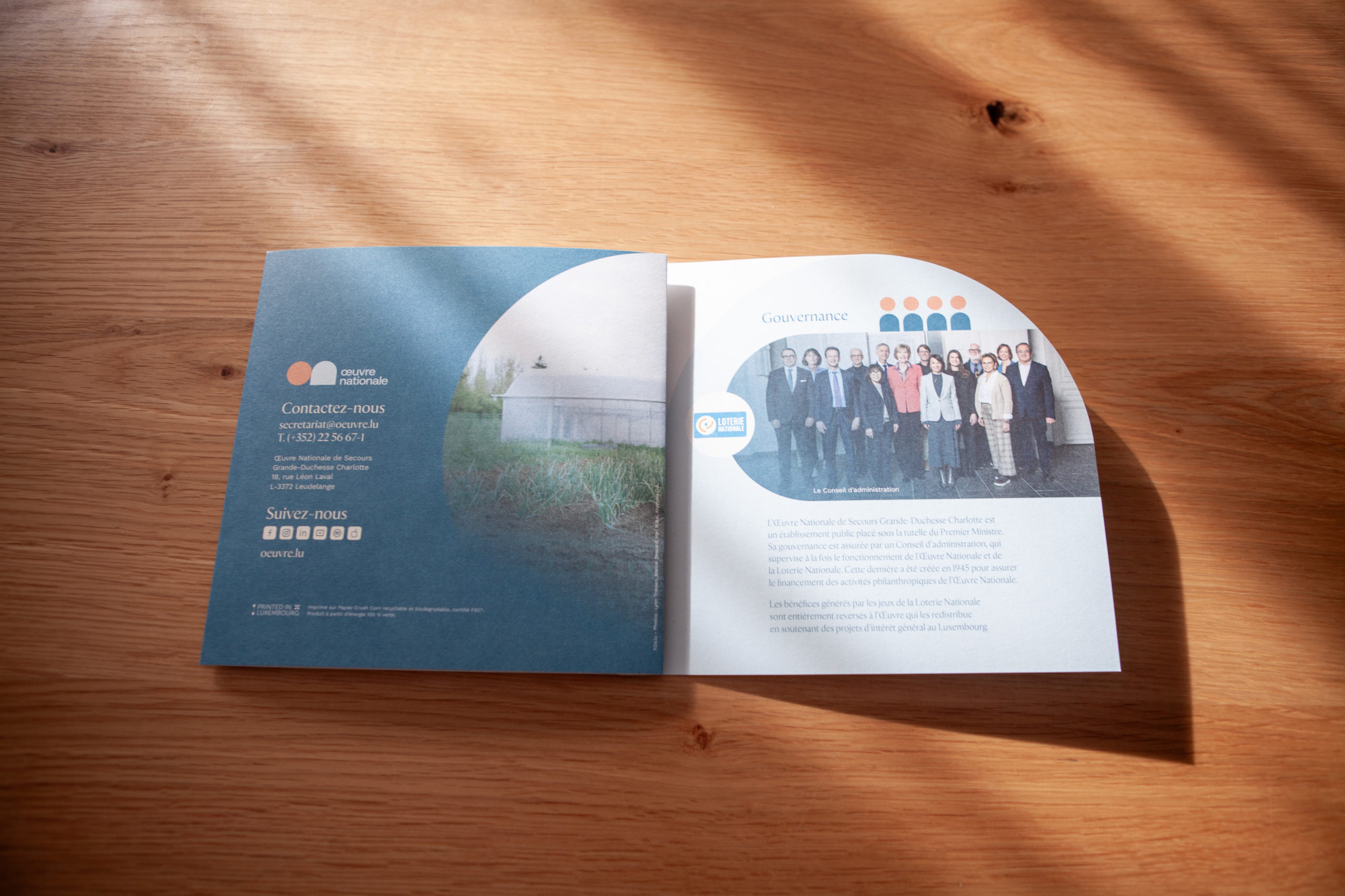 Brochure ouverte sur une table en bois avec une page de contact a gauche montrant une photo de terrain agricole et une page de gouvernance a droite avec un portrait de groupe dune equipe dirigeante.