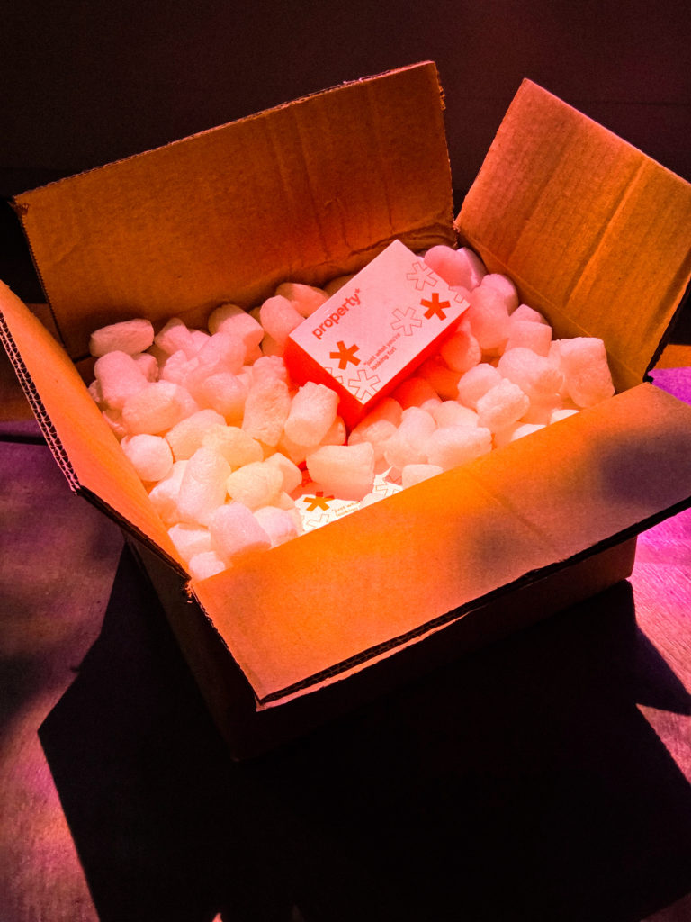 Colis d'expédition ouvert révélant le packaging orange de la marque Property soigneusement protégé par du calage.