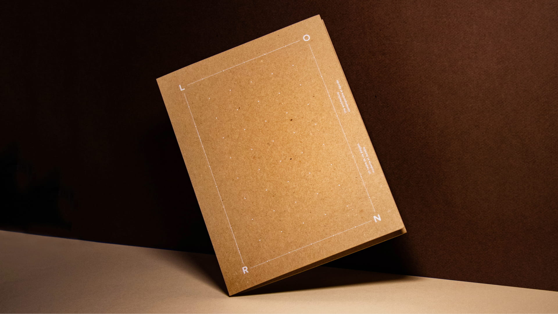 Brochure fermée en papier kraft avec un motif de points blancs et les lettres L, O, R et N dans les coins.