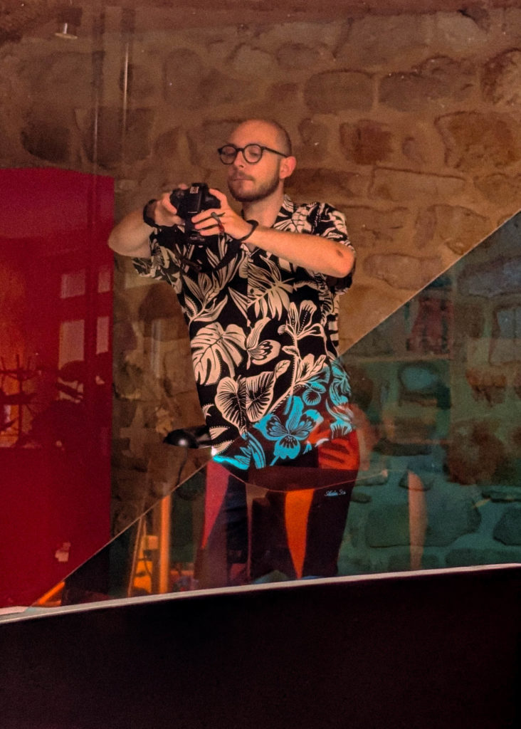 Reflet dans une vitre d'un homme en chemise à fleurs prenant une photographie avec un appareil professionnel.