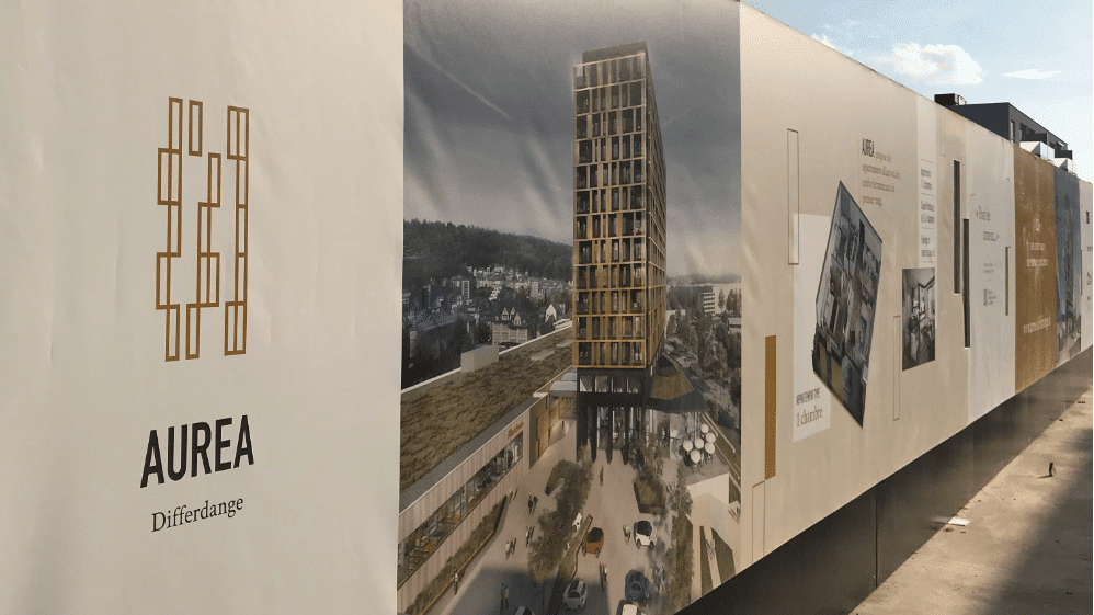Communication d'un projet immobilier illustrée par une palissade de chantier Aurea Differdange avec visuels architecturaux