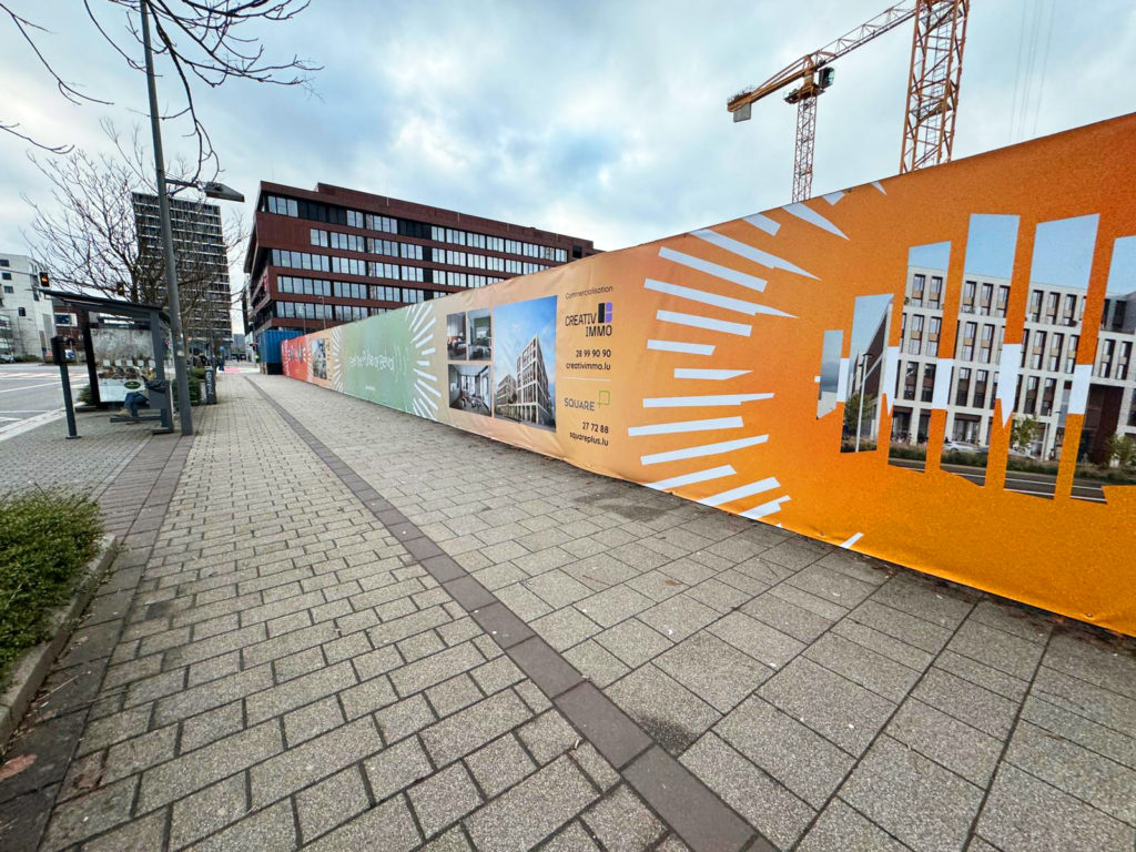 La palissade de chantier présente un design coloré et attrayant, mettant en avant les éléments clés du projet immobilier en construction. Chaque section est ornée d'illustrations et de visuels évoquant modernité et dynamisme, avec une communication claire des coordonnées et informations de contact de Creativ Immo, le promoteur. L'ensemble donne un aperçu de l'esthétique et de l'ambition du projet tout en apportant une touche vivante et professionnelle à l'environnement urbain.