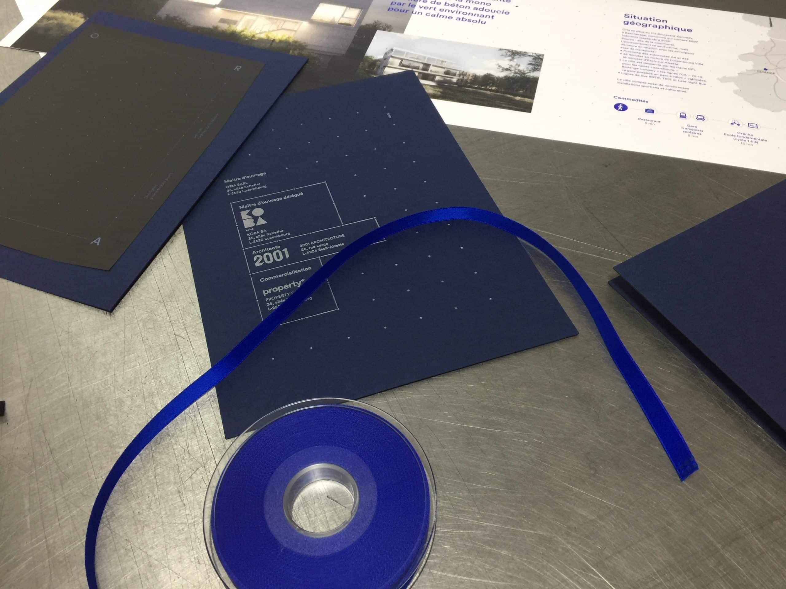 Table de travail avec plaquette Koba ouverte, coffret bleu et ruban assortis