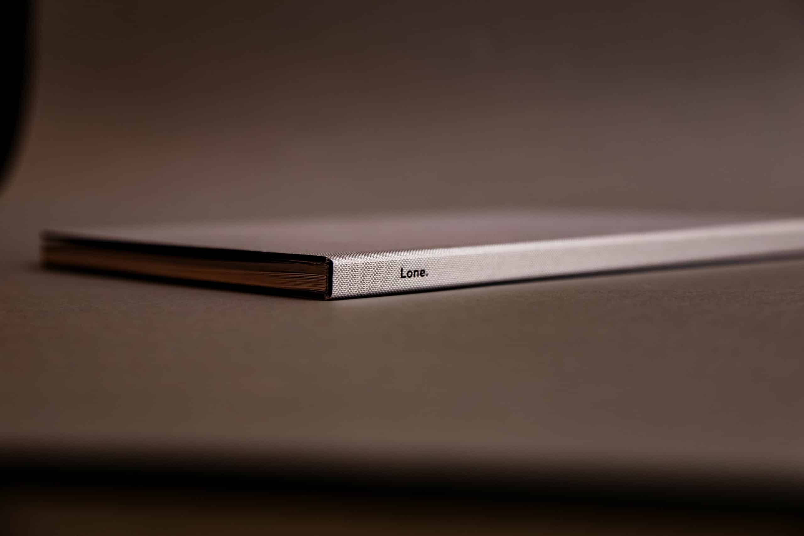 Détail de la tranche de la plaquette « Lone. », reliure textile grise