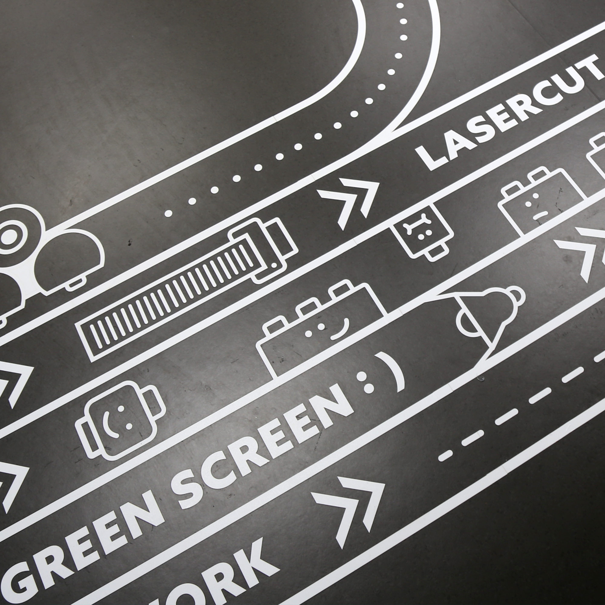 Signalétique directionnelle au sol du Makerspace guidant les élèves vers les espaces de création Lasercut et Green Screen.