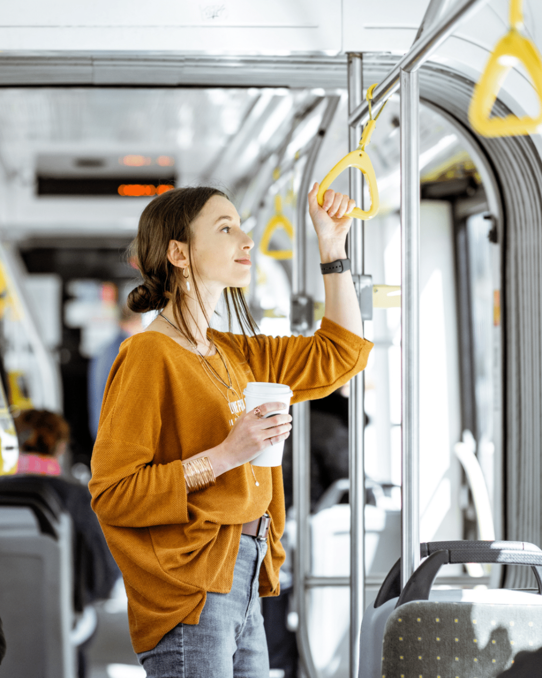 Passagère utilisant les transports en commun, debout dans l'allée centrale d'un bus lumineux en se tenant à une poignée de maintien.