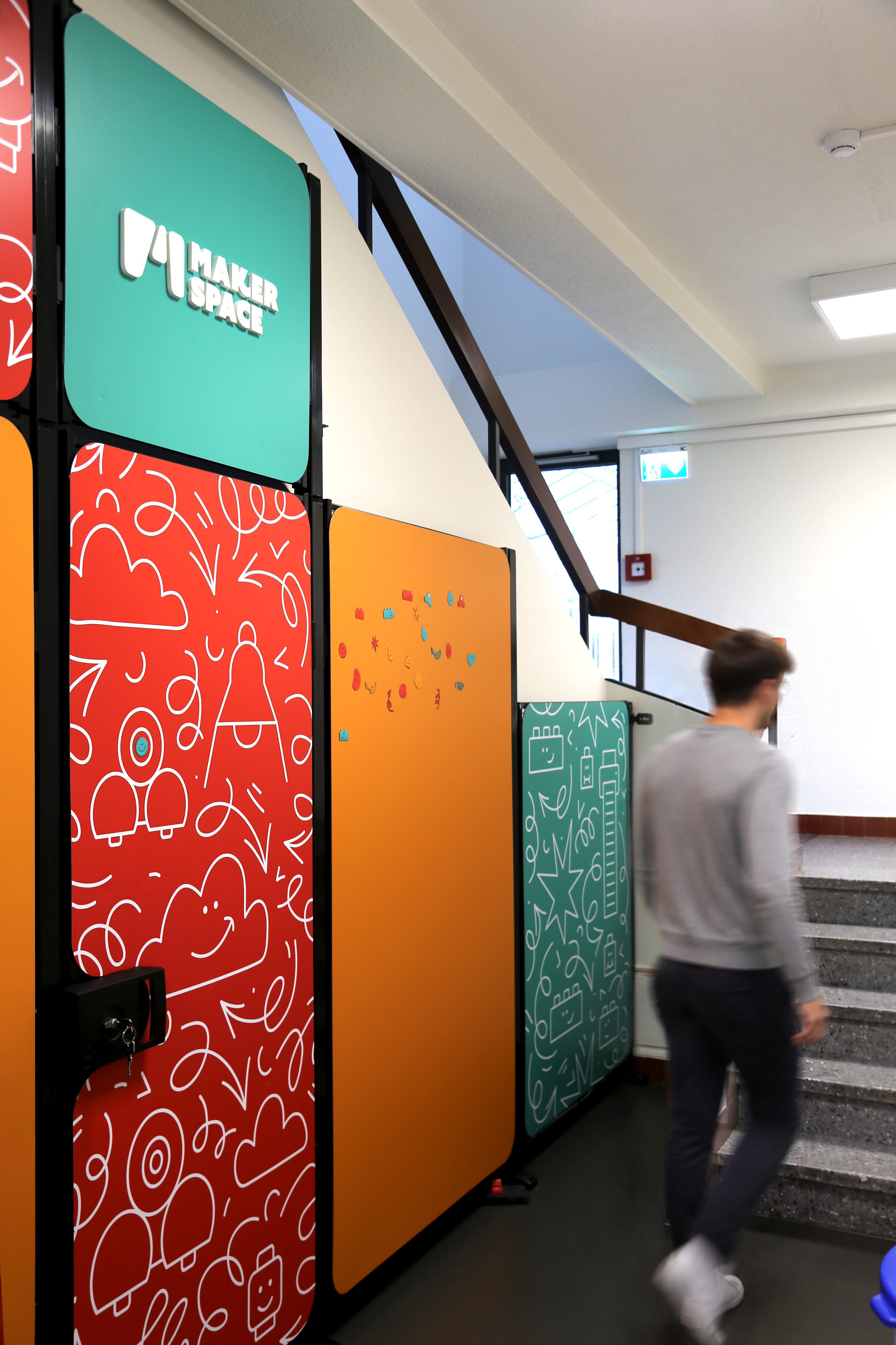 Un étudiant descendant les escaliers à côté de plusieurs panneaux muraux colorés du Maker Space.