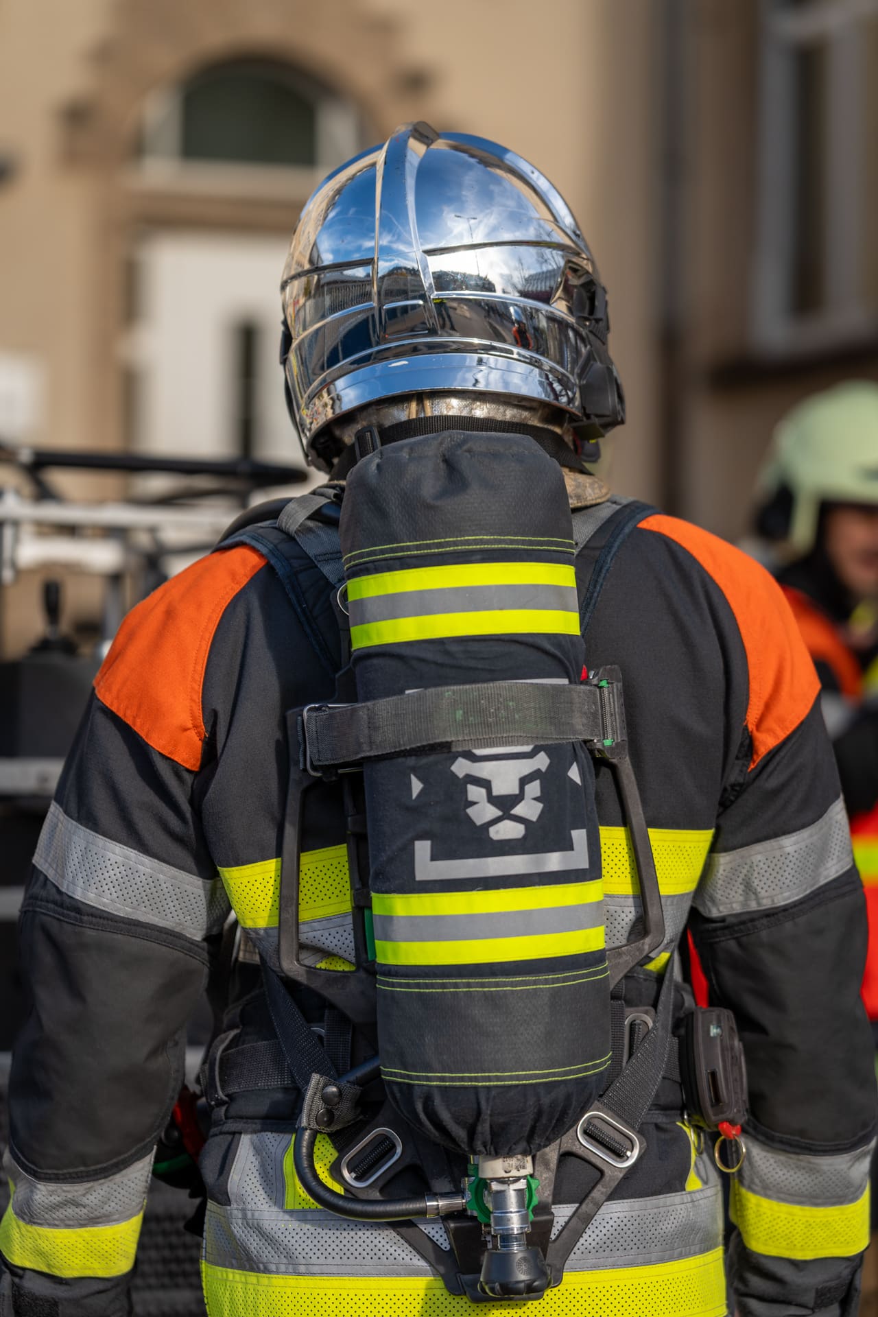 Pompier de dos en tenue d'intervention complète avec casque chromé et appareil respiratoire.