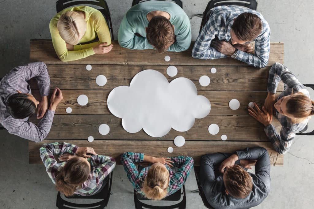Huit personnes assises autour d’une table en bois, en réunion, avec un dessin de nuage au centre représentant une idée ou un brainstorming