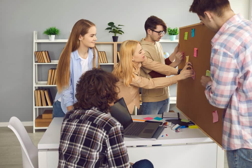 Groupe de collègues en réunion et épinglant des post-it sur un tableau en liège.