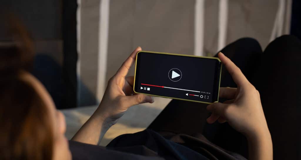 photographie d'une personne tenant son téléphone en horizontal et visionnant une vidéo
