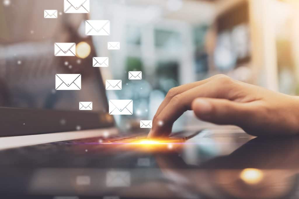 Main touchant un écran d’ordinateur portable avec des icônes d’e-mails flottants, représentant l’envoi ou la réception de courriels numériques