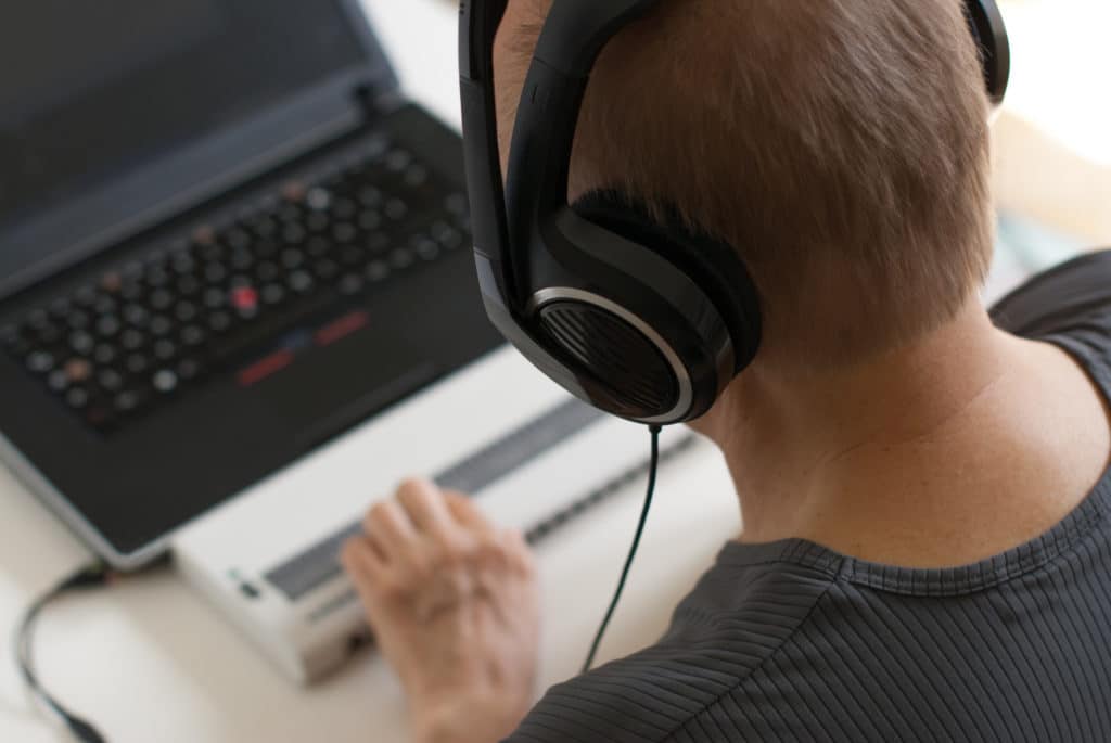 Un utilisateur malvoyant lit un PDF  accessibles sur un ordinateur portable à l’aide d’un afficheur braille et d’un casque audio.