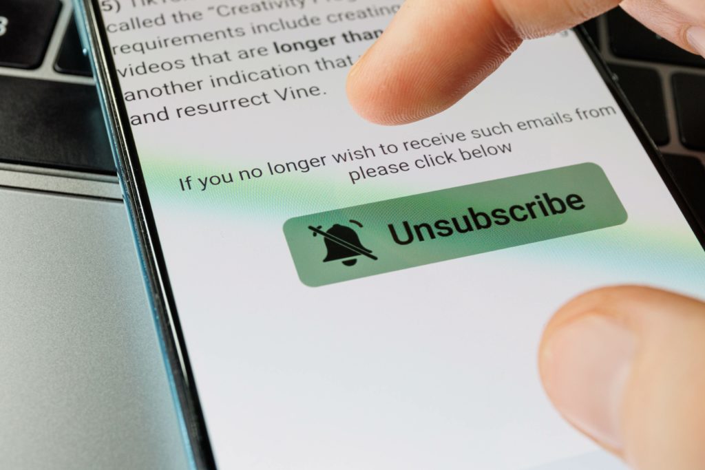 oigt sur un écran de smartphone appuyant sur un bouton vert Unsubscribe pour se désinscrire d’un e-mail.