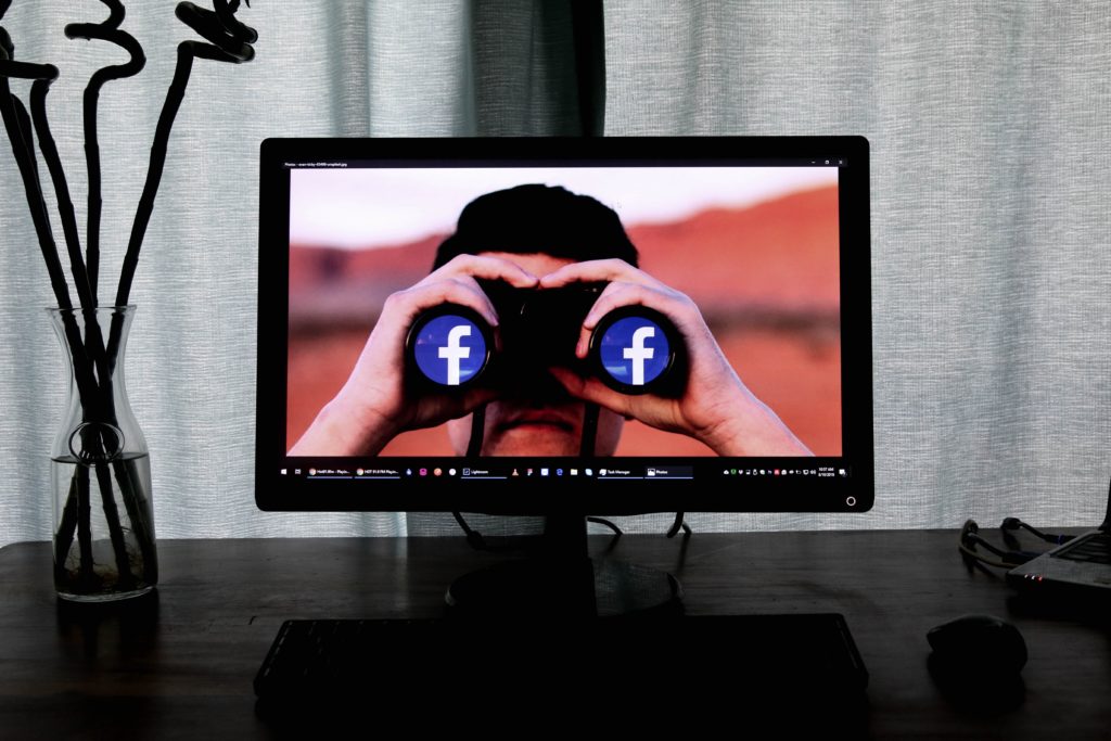 Écran d’ordinateur affichant un homme regardant à travers des jumelles avec le logo Facebook sur les lentilles