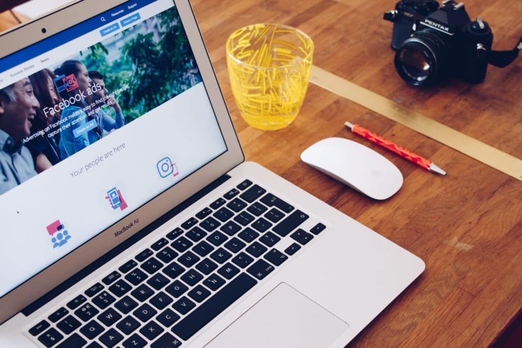 Ordinateur portable affichant Facebook Ads, posé sur un bureau avec une souris, un crayon, un pot de trombones et un appareil photo.
