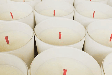 Gros plan de plusieurs bougies blanches alignées, chacune avec une mèche rouge, créant un effet visuel répétitif et harmonieux.