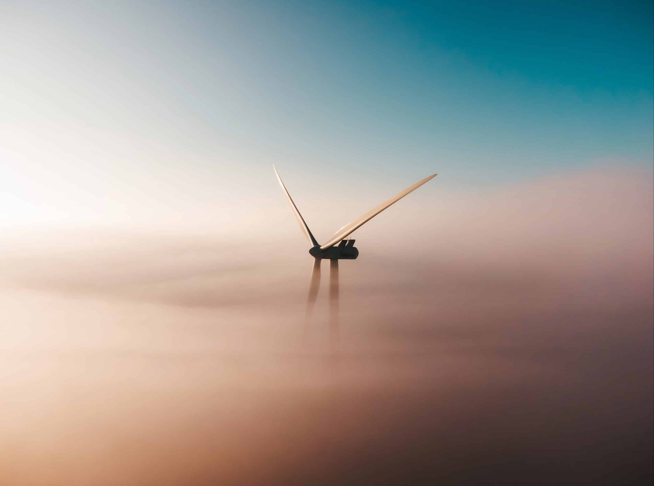 Paysage illustrant le secteur des énergies renouvelables avec une éolienne dépassant des nuages au lever du soleil.