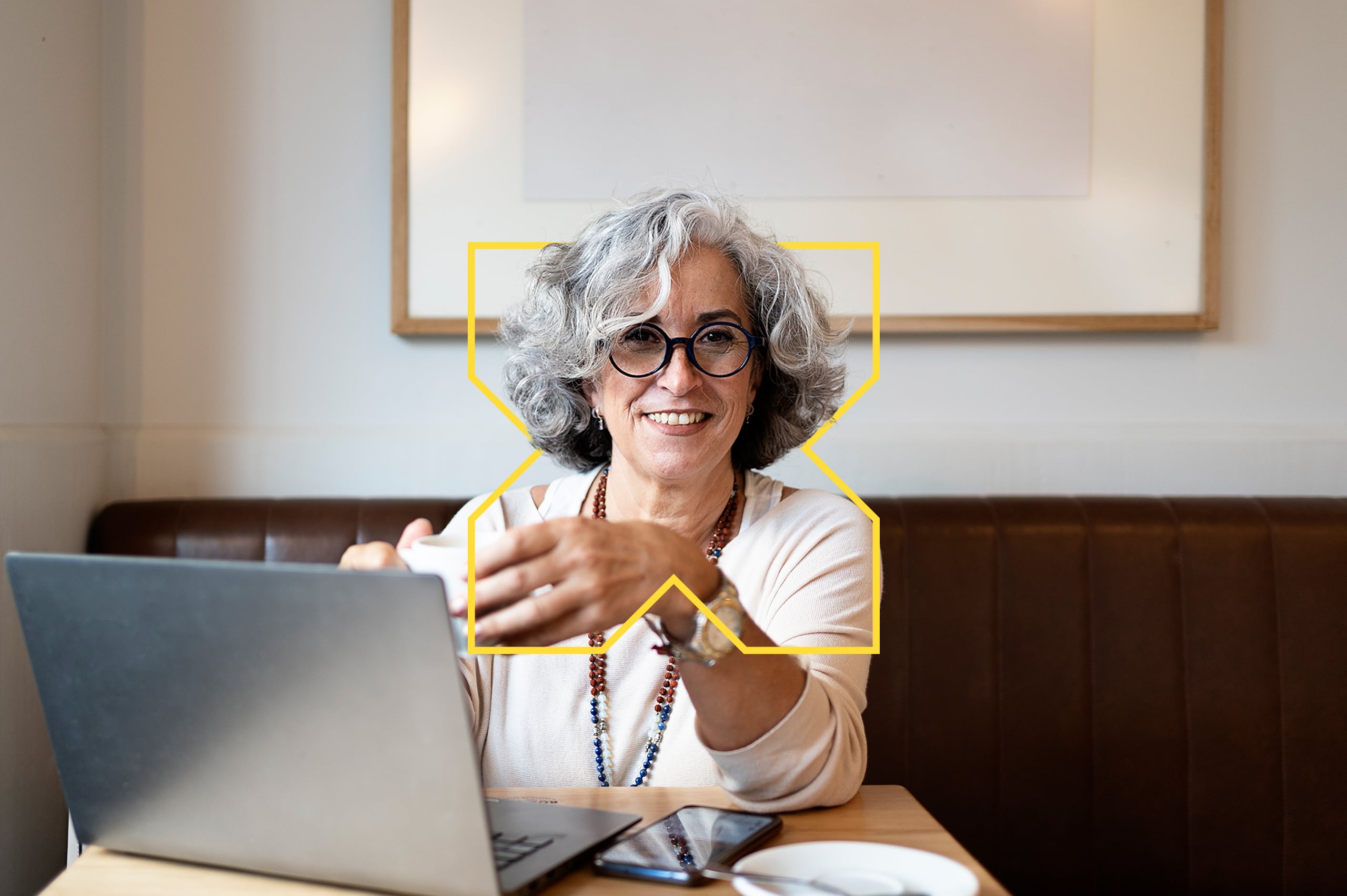 Femme senior souriante devant un ordinateur portable dans un café.