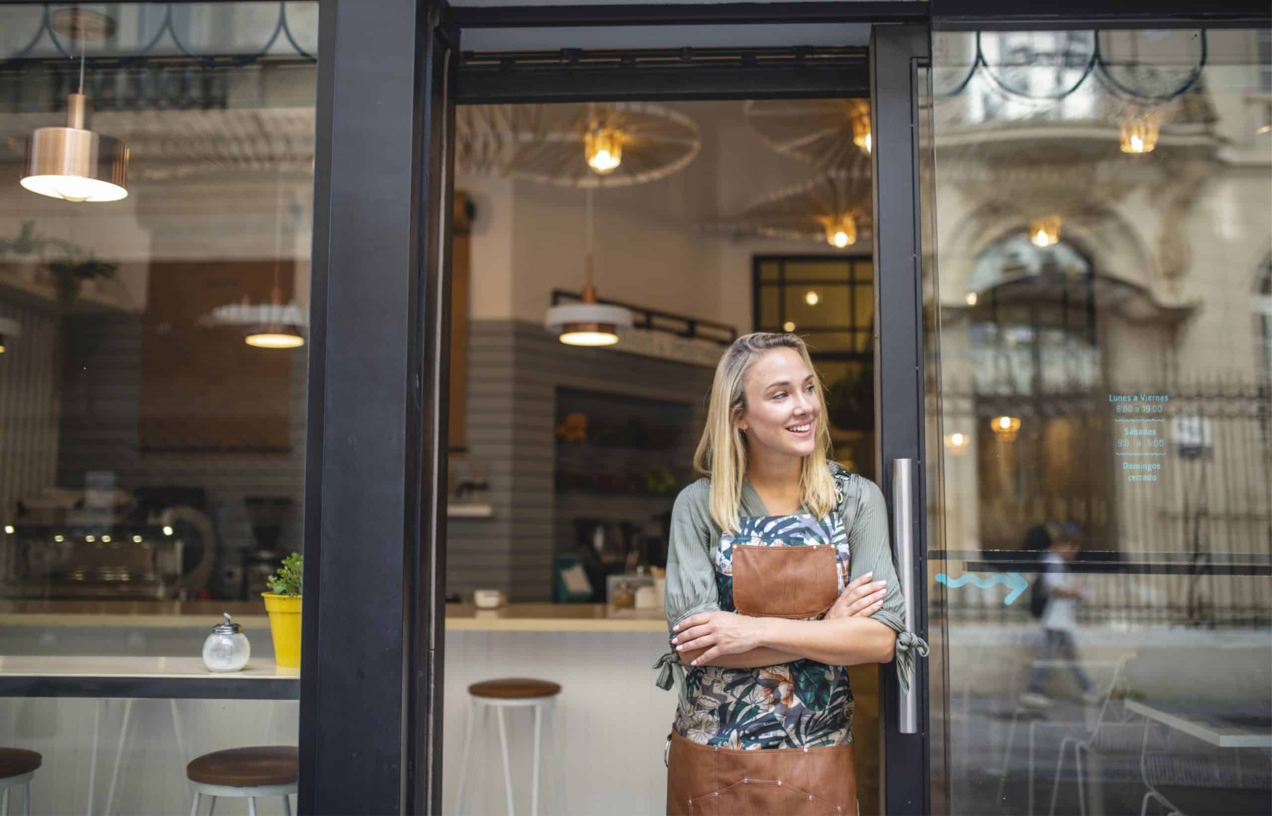 Femme commerçante souriante debout devant l’entrée de sa boutique.