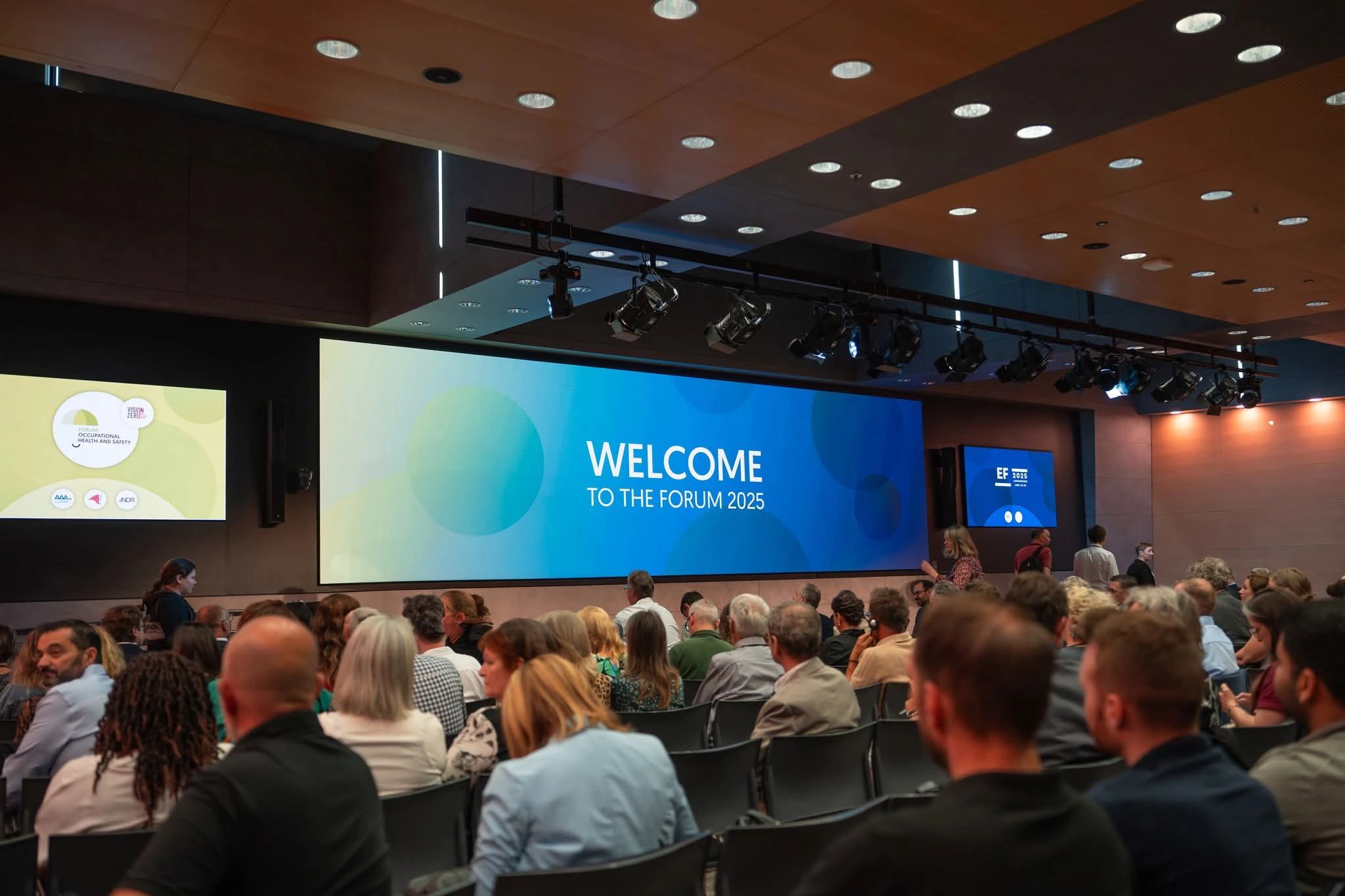 Conférence en cours au Forum 2025 avec une salle remplie de participants, face à un écran indiquant 'Welcome to the Forum 2025'.