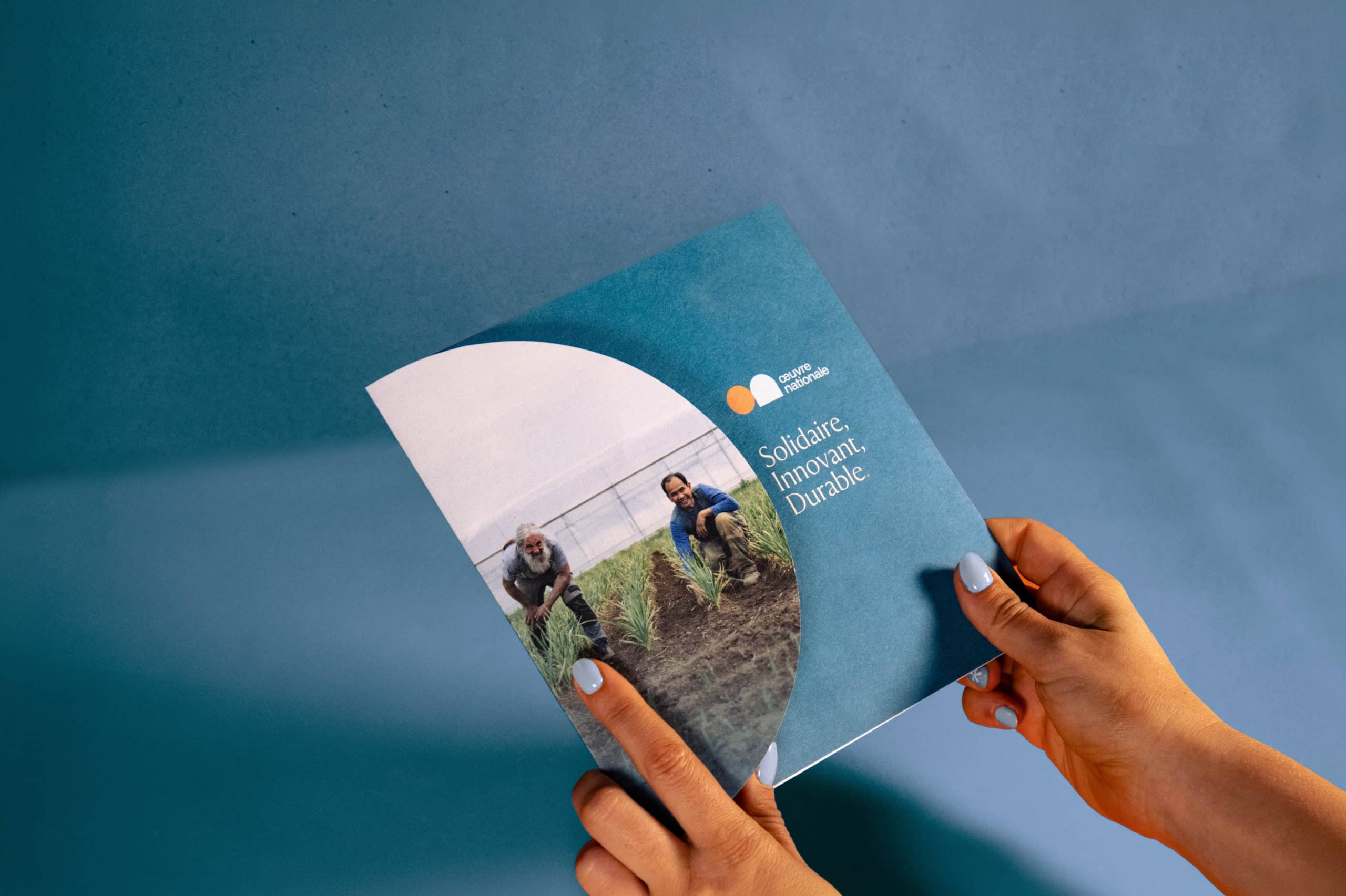 Couverture de la brochure de l'Œuvre Nationale tenue en main, affichant les valeurs Solidaire, Innovant et Durable.