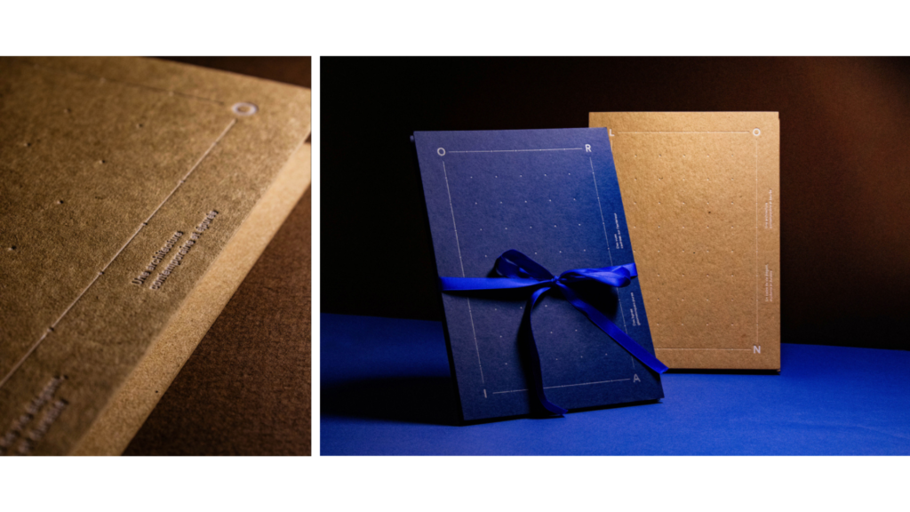 Deux brochures KOBA posées debout ; au premier plan une brochure bleu foncé nouée d'un ruban bleu satiné, au second plan une brochure en papier kraft.