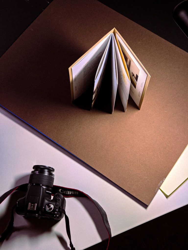 Brochure pliée en accordéon tenue debout sous un éclairage directionnel de studio, à côté d'un appareil photo.