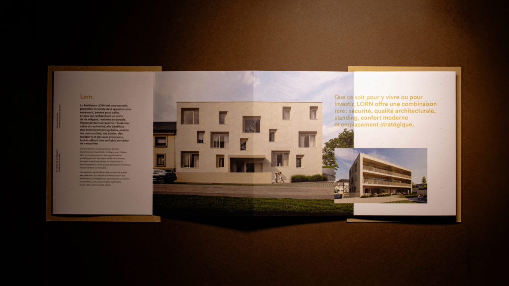 Brochure LORN entièrement dépliée en trois volets, présentant un texte de présentation à gauche, le rendu 3D d'une résidence blanche aux fenêtres asymétriques au centre, et un résumé des atouts d'investissement à droite.
