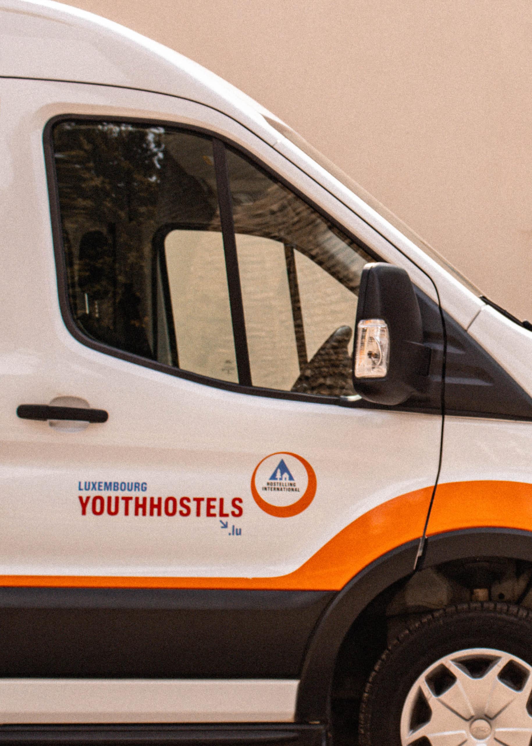 Portière d'une camionnette blanche arborant le logo et les couleurs orange de Luxembourg Youth Hostels.