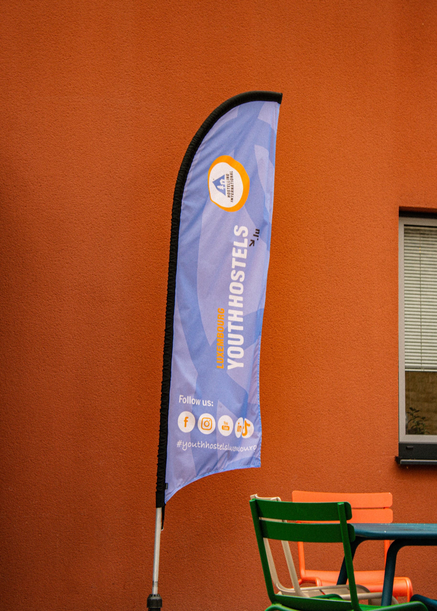 Oriflamme promotionnel bleu des auberges de jeunesse du Luxembourg invitant les visiteurs à utiliser le hashtag youthhostelsluxembourg sur les réseaux sociaux.