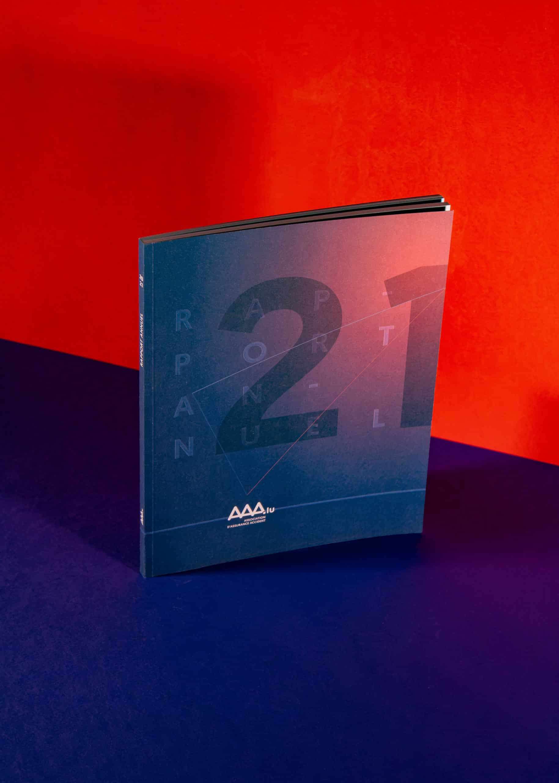 Édition imprimée du rapport annuel 2021 de l'Association d'Assurance Accident, design géométrique sur fond rouge et bleu.