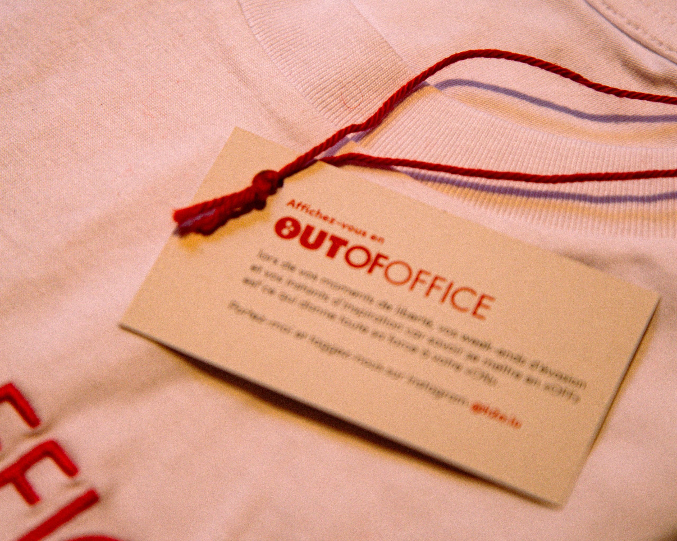 Mains ouvrant un colis rouge contenant un t-shirt blanc et une carte de remerciement.
